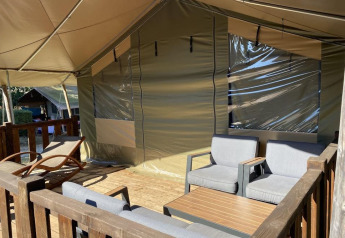 Terrasse extérieure d'une tente safari avec fauteuils confortables, table en bois et chaise longue relaxante.
