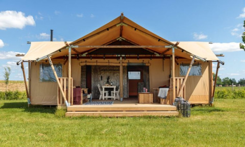 Safaritent Bella Lodge, une grande tente safari sur un champ d’herbe verte sous un ciel bleu et ensoleillé.