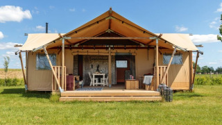 Safaritent Bella Lodge, een ruime safaritent lodge op grasveld onder een blauwe lucht en zonnig weer.