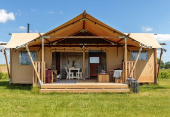 Safaritent Bella Lodge, a spacious safari tent lodge on a grassy field under blue sky and sunshine.