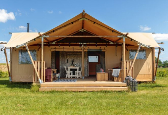 Safaritent Bella Lodge, une grande tente safari sur un champ d’herbe verte sous un ciel bleu et ensoleillé.