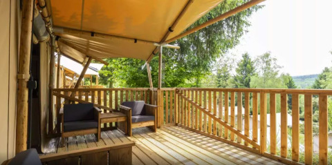 Terrasse en bois avec coin salon à Safaritent Bella Lodge, Camping Valkanela, entourée de verdure.