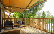 Terrasse en bois avec coin salon à Safaritent Bella Lodge, Camping Valkanela, entourée de verdure.
