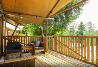 Terrasse en bois avec coin salon à Safaritent Bella Lodge, Camping Valkanela, entourée de verdure.