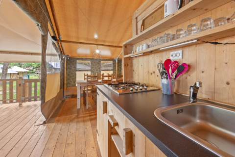 Cocina en tienda safari con interior de madera, fogón y comedor en Camping Polari, Croacia.