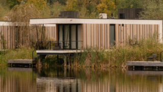 Moderna Waterlodge Sauna en Resort de Parel, Países Bajos, con vistas al lago y rodeada de árboles otoñales.