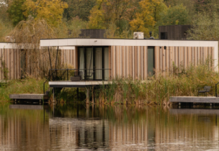 Moderne Waterlodge Sauna im Resort de Parel, Niederlande, am Wasser mit Herbstbäumen im Hintergrund.