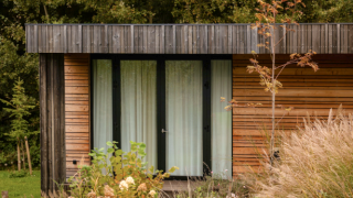 Eine Lodge mit moderner Holzfassade, großen Fenstern und umgeben von üppigen Büschen und Gräsern.