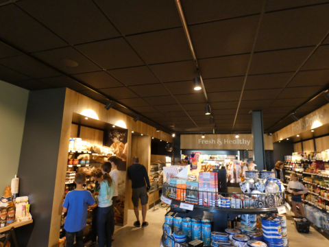 Gasten winkelen in een glamping-winkel met schappen vol verse producten, drankjes en diverse snacks.