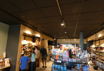 Ospiti fanno acquisti in un moderno market di glamping con cibi freschi, snack e bevande sugli scaffali.