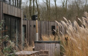 Udendørs terrasse med træbænk, bord, jacuzzi og højt græs ved en moderne lodge i Resort de Parel, Holland.