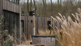 Houten terras met picknicktafels en hottub tussen hoog gras bij moderne lodge in Resort de Parel, Nederland.