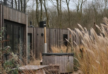 Houten terras met picknicktafels, hottub en hoog gras bij een moderne lodge in Resort de Parel, Nederland.