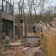 Houten terras met picknicktafels en hottub tussen hoog gras bij moderne lodge in Resort de Parel, Nederland.