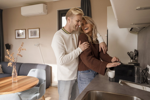 Jeune couple partageant un moment complice dans la cuisine moderne d’un lodge en préparant un café.