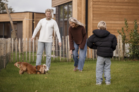 Gezin speelt met hond in de tuin van Parklodge 4 met hondenhek, sauna en hottub in Nederland.