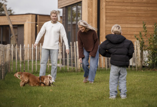Gezin speelt met hun hond in de tuin bij Parklodge 4 met hondenhek, sauna en hottub in Nederland.