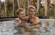 Ein Paar entspannt gemeinsam im Outdoor-Whirlpool an einer Lodge, umgeben von Natur und Bäumen.