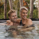 Couple enjoying relaxing time together in an outdoor hot tub at a lodge with nature in the background.