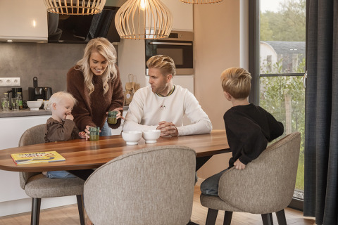 Une famille de quatre personnes prend le petit-déjeuner ensemble dans une cuisine moderne et chaleureuse de lodge.