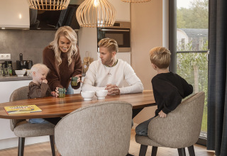 Une famille de quatre personnes prend le petit-déjeuner ensemble dans une cuisine moderne et chaleureuse de lodge.