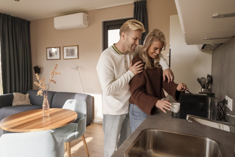 A young couple enjoys making coffee together in the kitchen of a modern, cozy lodge setting.