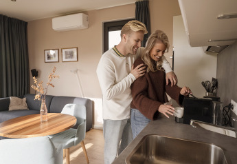Et ungt par nyder tid sammen i køkkenet på en moderne lodge, mens de laver kaffe om morgenen.