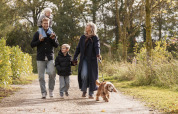 Family with two children and a dog walking together along a forest path near a lodge on a sunny day.