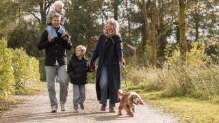 Family with two children and a dog walking together along a forest path near a lodge on a sunny day.