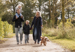 Familie med to børn og en hund går sammen på en skovsti i nærheden af et lodge på en solrig dag.