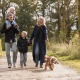 Familie med to børn og en hund går sammen på en skovsti i nærheden af et lodge på en solrig dag.