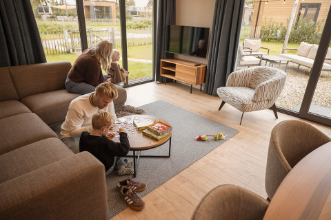 Familie hygger sig i en moderne lodge med store vinduer, leger puslespil og nyder udsigten udenfor.