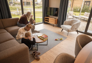 Familie hygger sig i en moderne lodge med store vinduer, leger puslespil og nyder udsigten udenfor.