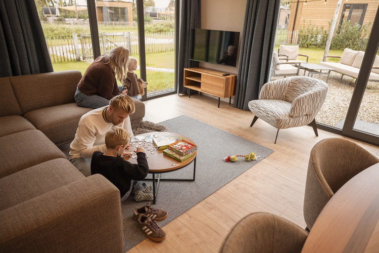 Family enjoys a modern lodge with large windows, playing a puzzle game together and relaxing indoors.