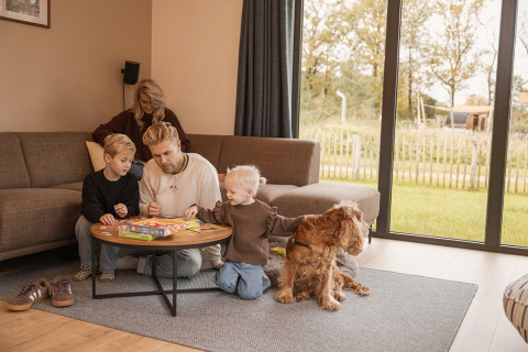 Familie hygger sig i opholdsstuen med brætspil og deres hund på Holiday villa Amalia i Hofparken Wiltershaar.