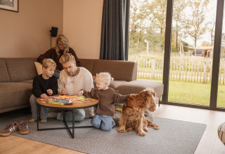 Familie hygger sig i opholdsstuen med brætspil og deres hund på Holiday villa Amalia i Hofparken Wiltershaar.
