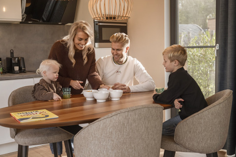 Family enjoys a moment together at the dining table in Holiday Villa Amalia at Hofparken Wiltershaar, Netherlands.