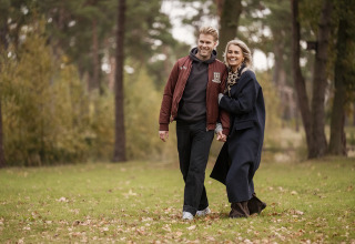 Pareja paseando por el césped junto a Holiday villa Amalia 2 con sauna y jacuzzi en Hofparken Wiltershaar, Países Bajos.