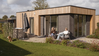 Twee personen genieten buiten Water lodge 2 Deluxe met sauna, hot tub, tuin en hond op het gras.