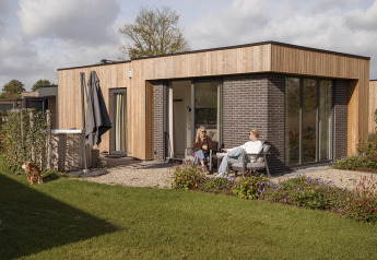 Two people relaxing outside Water lodge 2 Deluxe with sauna and hot tub, garden and a dog in the yard.
