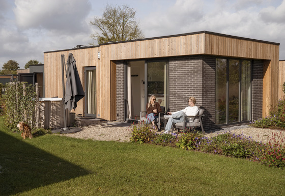 Two people relaxing outside Water lodge 2 Deluxe with sauna and hot tub, garden and a dog in the yard.