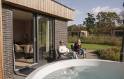 Moderne Lodge mit zwei Personen, die sich draußen am Whirlpool bei Hofparken Wiltershaar, Niederlande entspannen.