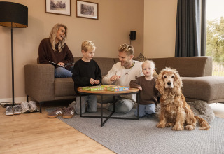 Una familia se relaja junta en la sala de una cabaña acogedora, jugando y acompañados de su perro.