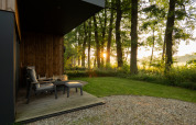 Zicht vanaf Vakantievilla Boslodge 2 in Hofparken Wiltershaar, Nederland, met terrasstoelen bij zonsopgang.