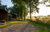 Ochtendlicht op een houten vakantielodge bij Hofparken Wiltershaar, tussen bomen en groene natuur.