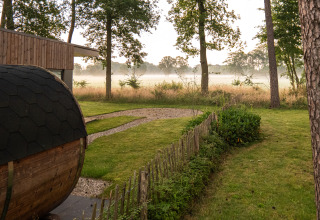 Foto af en lodge med en græsplæne, træer og let morgentåge over marken i baggrunden.