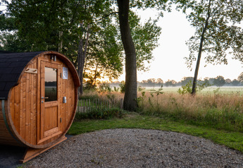 Houten barrelsauna bij Vakantievilla Boslodge 2 met sauna op Hofparken Wiltershaar in Nederland bij zonsopgang.