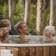 Eine lächelnde Familie entspannt in einem Outdoor-Whirlpool aus Holz in natürlicher Umgebung bei einer Lodge.