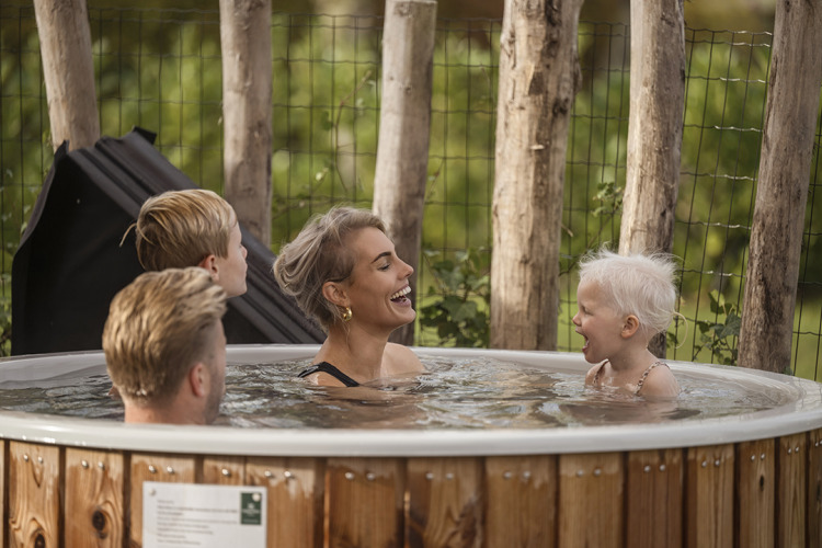 Una familia sonriente disfruta de una bañera de hidromasaje al aire libre rodeada de árboles en una cabaña.