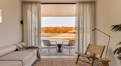 Salotto moderno e luminoso in una Waterlodge al Resort de Parel, Paesi Bassi, con vista lago e bosco autunnale.